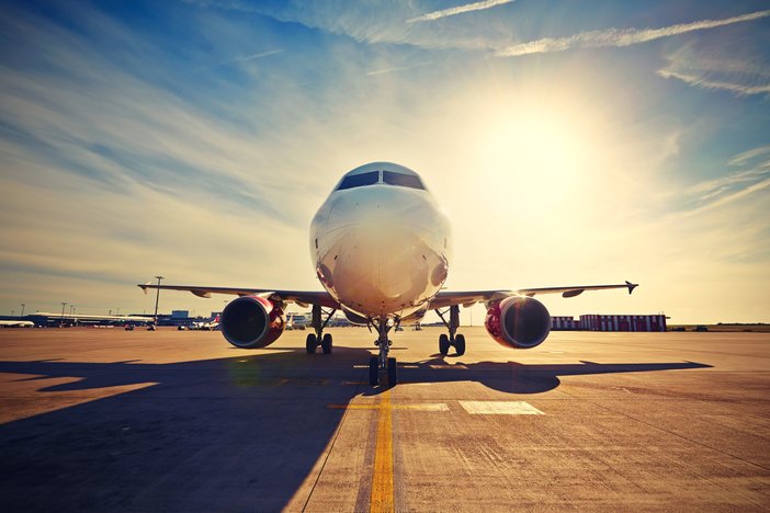 Front view of a large white passenger jet parked on the runway with the sun behind it.